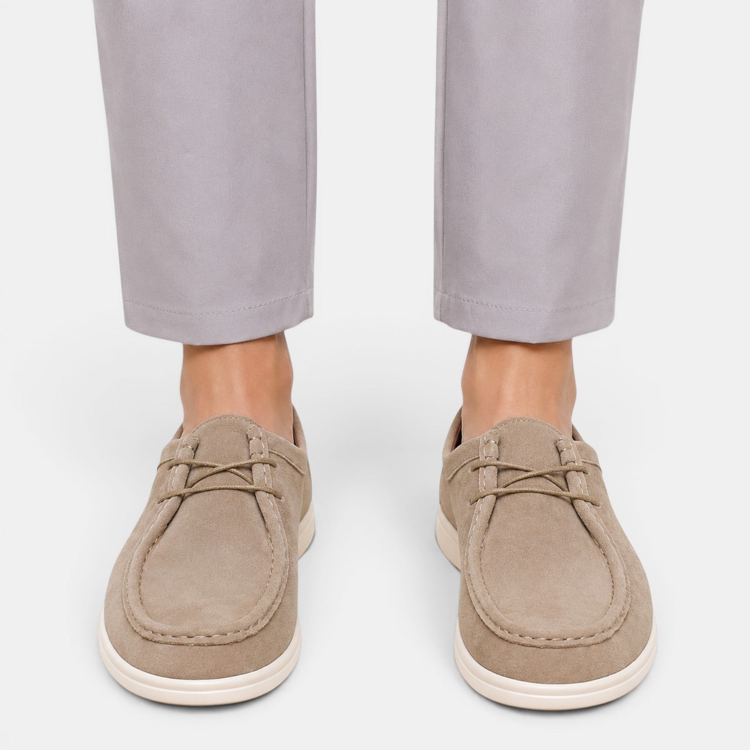 Person wearing beige suede lace-up shoes with white soles and light gray trousers, viewed from the front.