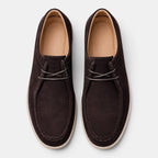 Top view of a pair of dark brown suede lace-up shoes with white soles against a light gray background.