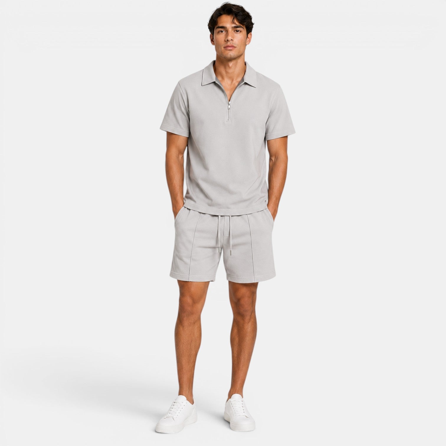 Man wearing a light gray zip-collar polo shirt with matching drawstring shorts and white sneakers, standing against a light gray background.