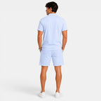 Back view of a man wearing a light blue polo shirt, matching shorts, and white sneakers against a light gray background.