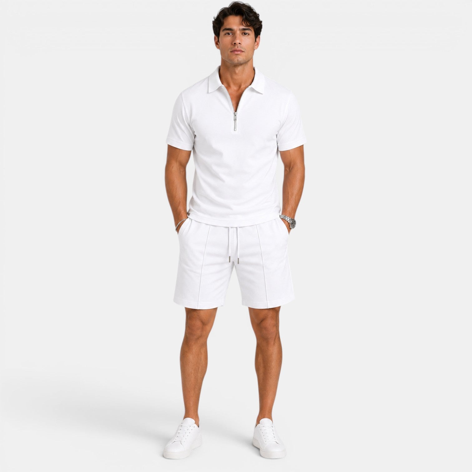 Man wearing a white zip-collar polo shirt with matching drawstring shorts and white sneakers, standing against a light gray background.