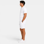 Side view of a man wearing a white zip-collar polo shirt, matching shorts, and white sneakers against a light gray background.