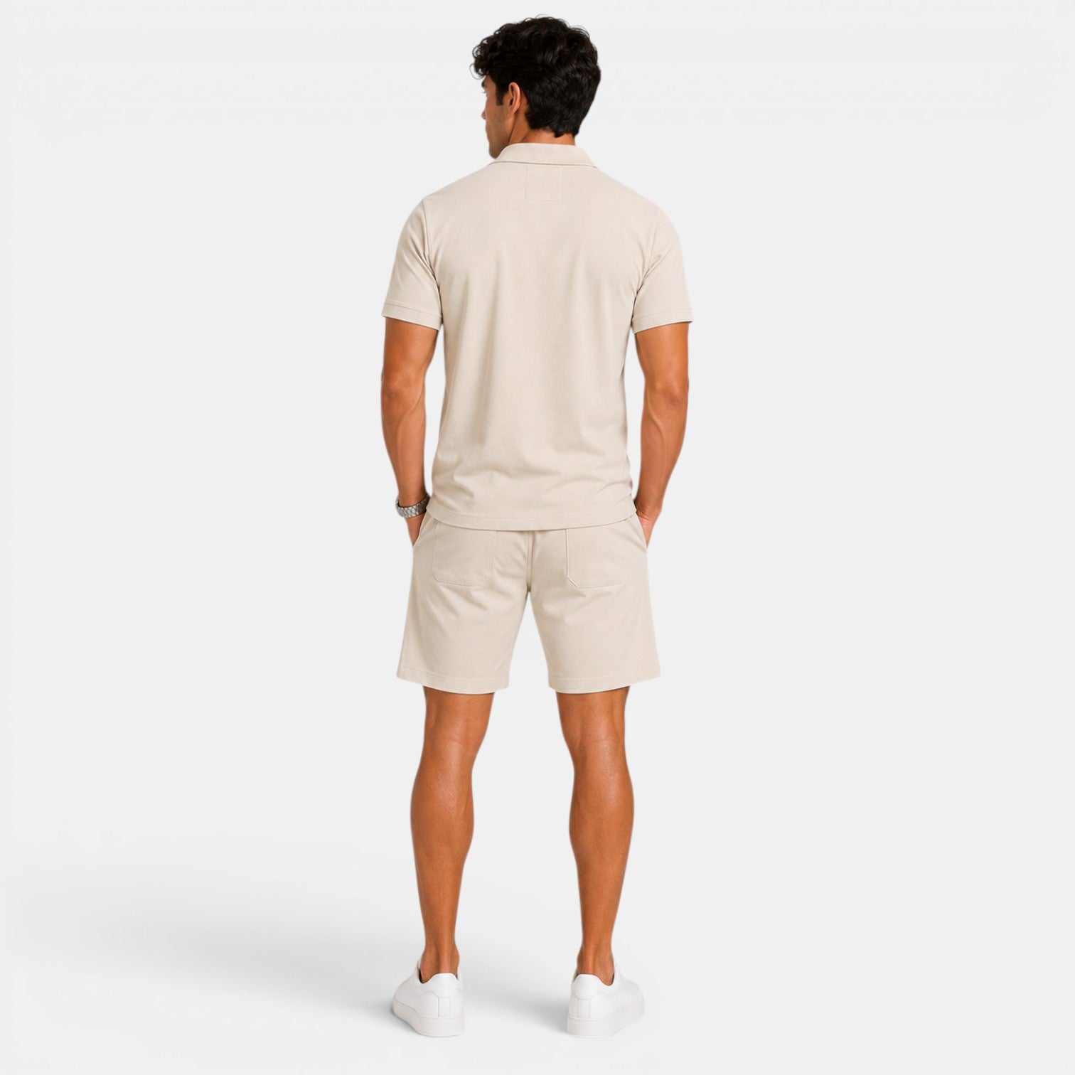 Back view of a man wearing a beige polo shirt, matching shorts, and white sneakers against a light gray background.