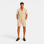 Man wearing a beige outfit with shorts and a shirt on a white background
