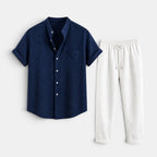 Navy short-sleeve button-up shirt paired with white drawstring trousers, displayed against a light gray background.