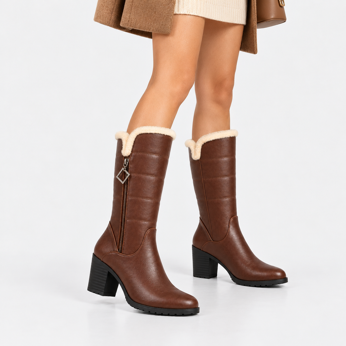 A pair of brown mid-calf boots with a cream faux-fur trim and a block heel, shown on a model against a light gray studio background.