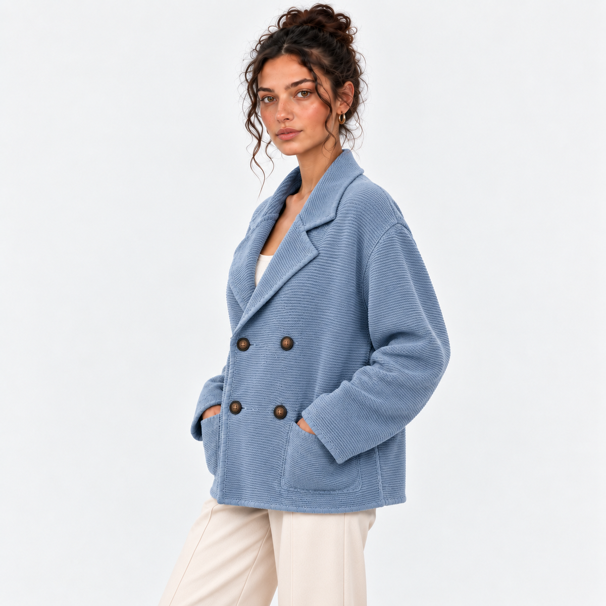 Side view of a woman wearing a light blue double-breasted knit blazer with white pants