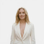 Woman wearing a white blazer with a plunging neckline on a plain background