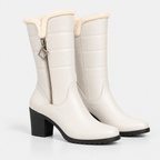 A pair of off-white faux leather mid-calf boots with a black block heel and a cream-colored shearling lining at the collar, shown on a light gray background.