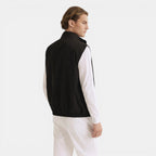 Man wearing a black vest over a white shirt on a light gray background