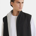 Man wearing a black vest over a white shirt on a light gray background