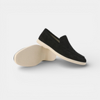 Black loafers with beige soles on a light gray background