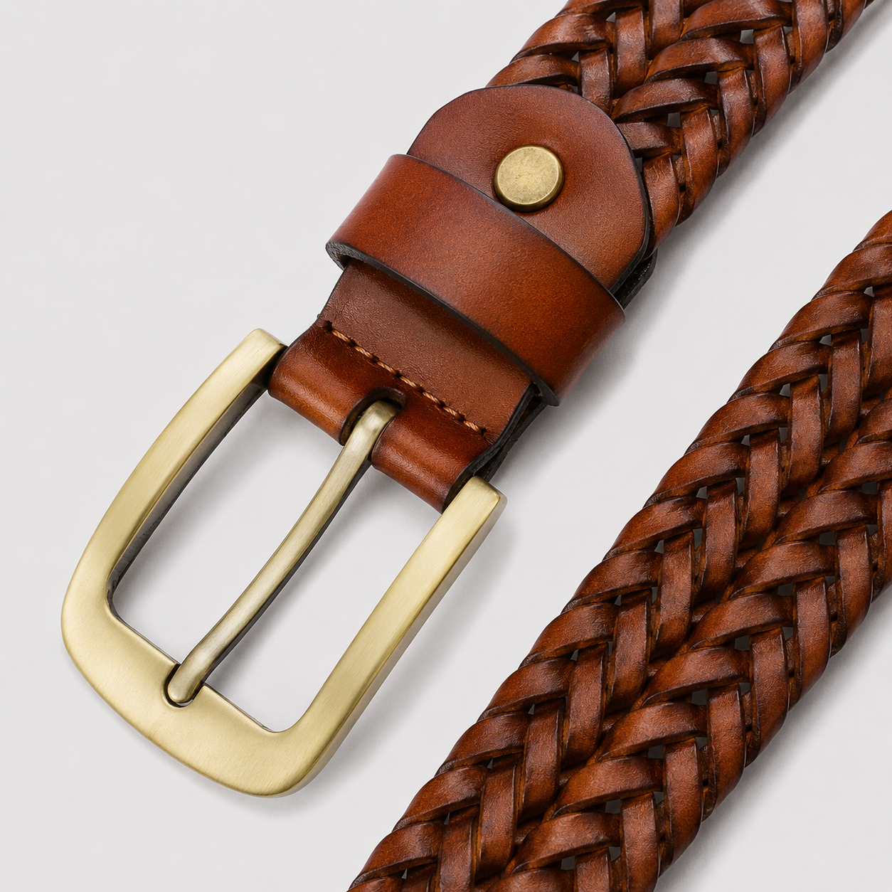 A close-up of a brown braided leather belt with a brass buckle and a small brass rivet, shown on a light gray background.