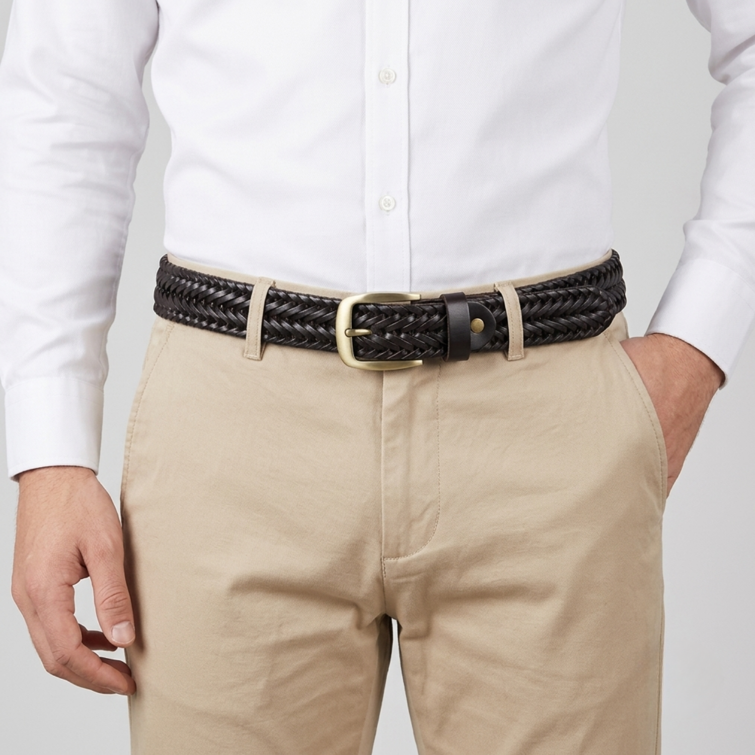 A close-up of a man wearing a black braided leather belt with a gold-tone buckle, paired with beige trousers and a white dress shirt.