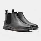 A pair of black leather Chelsea boots with elastic side panels and pull tabs, shown on a light gray background.