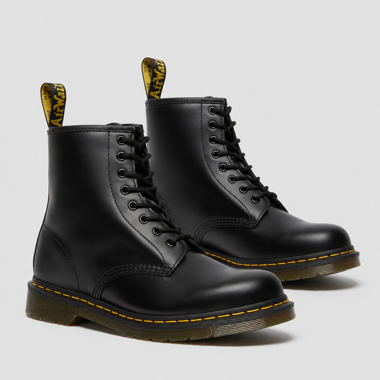 A pair of classic black leather Dr. Martens 1666 boots with yellow stitching and pull tabs, shown on a light gray background.
