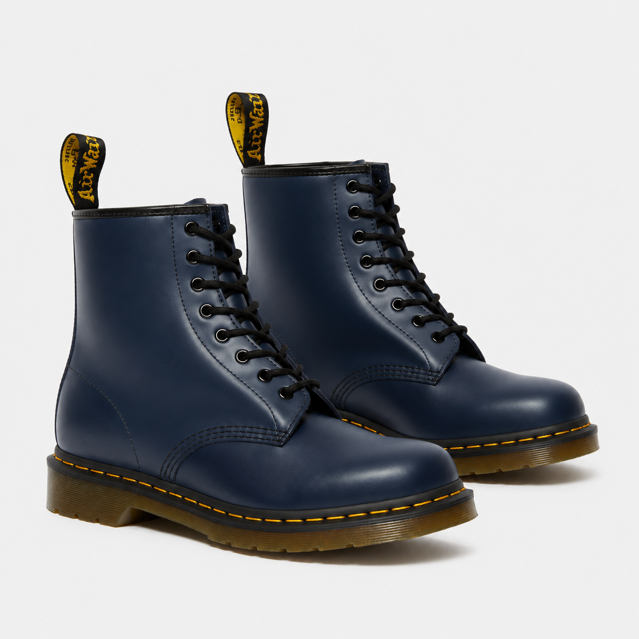 A pair of navy blue Dr. Martens 1-864 boots with black laces, yellow stitching, and a brown sole, shown on a light gray background.