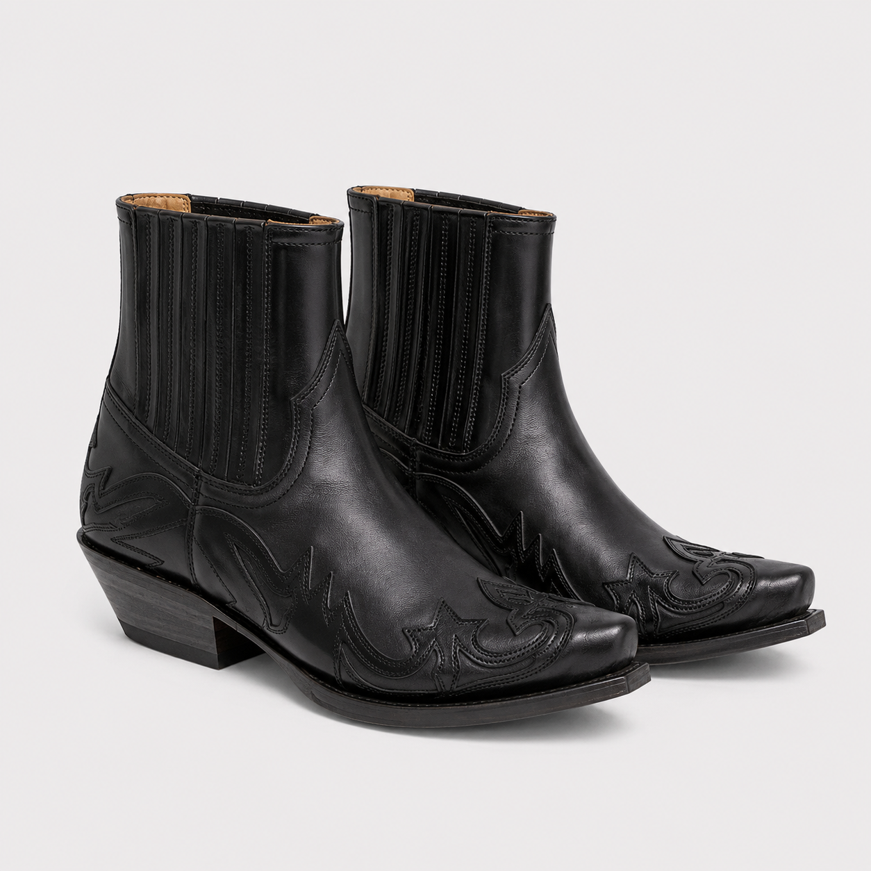 A pair of black leather ankle boots with western-style stitching, embossed floral details on the toes, and elastic side panels, shown against a light gray background.