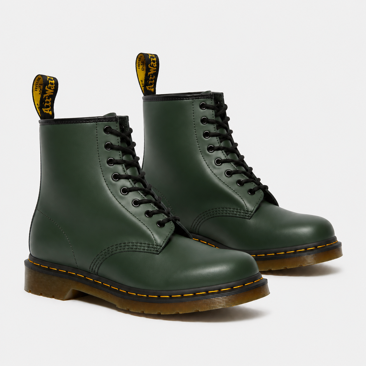 A pair of classic Dr. Martens 1-8-inch ankle boots in dark forest green leather, featuring black laces, yellow stitching, and the signature yellow heel pull tabs with black branding.