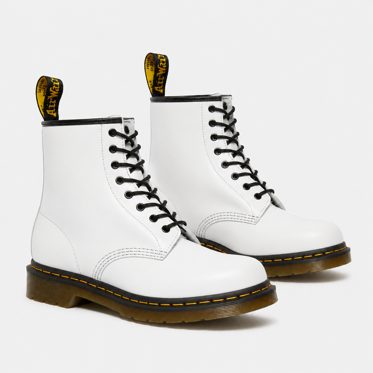 A pair of white Dr. Martens 16-eyelet lace-up boots with black laces, black trim, and a classic yellow welt and heel pull tabs, shown on a light gray background.