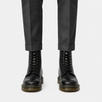 Black lace-up leather boots worn with dark gray cuffed trousers, shown from the front on a light gray background.