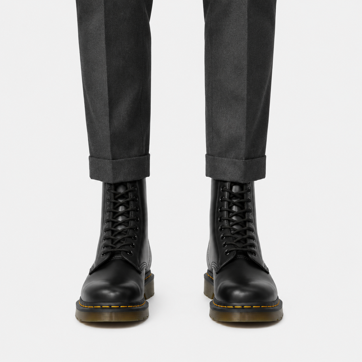 Black lace-up leather boots worn with dark gray cuffed trousers, shown from the front on a light gray background.