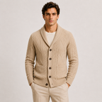 A man wearing a beige cable-knit cardigan sweater over a white t-shirt and beige trousers, standing against a light gray studio background.