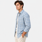 A man wearing a light blue and white checkered long-sleeve button-down shirt over a white undershirt, paired with beige pants, photographed against a solid white background.