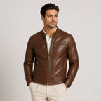A man wearing a brown leather jacket with zippered chest pockets and a front zipper, paired with light beige trousers, photographed against a plain light gray studio background.