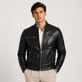 A man wearing a black leather moto jacket over a white collared shirt and beige trousers, standing against a light gray studio background.