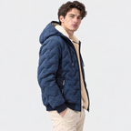 A man wearing a navy blue quilted puffer jacket with a beige sherpa lining, paired with beige pants, photographed against a light gray studio background.