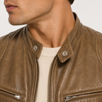Close-up of a man wearing a brown leather jacket over a cream ribbed sweater, showing the collar, front zipper, and chest pockets.