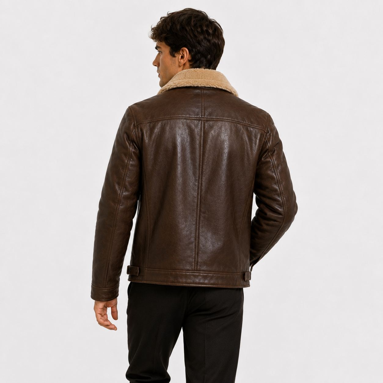 A man viewed from the back wearing a dark brown leather jacket with a beige sherpa collar, paired with black pants, against a plain light gray studio background.