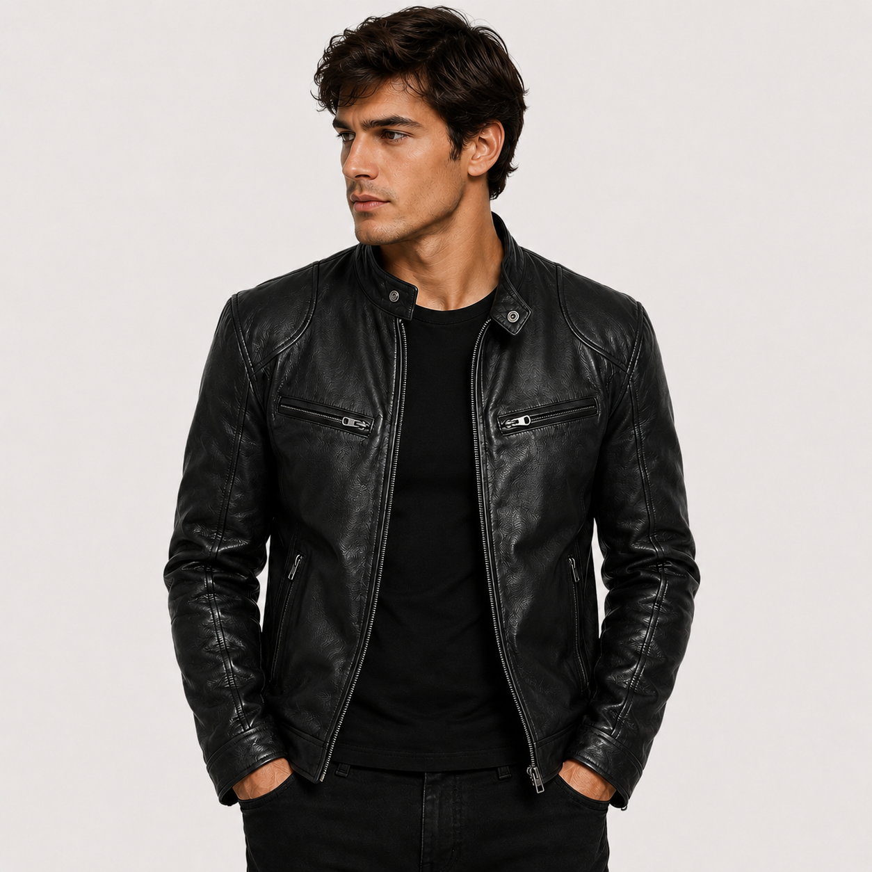 A man wearing a black leather motorcycle jacket over a black t-shirt, standing against a light gray studio background.