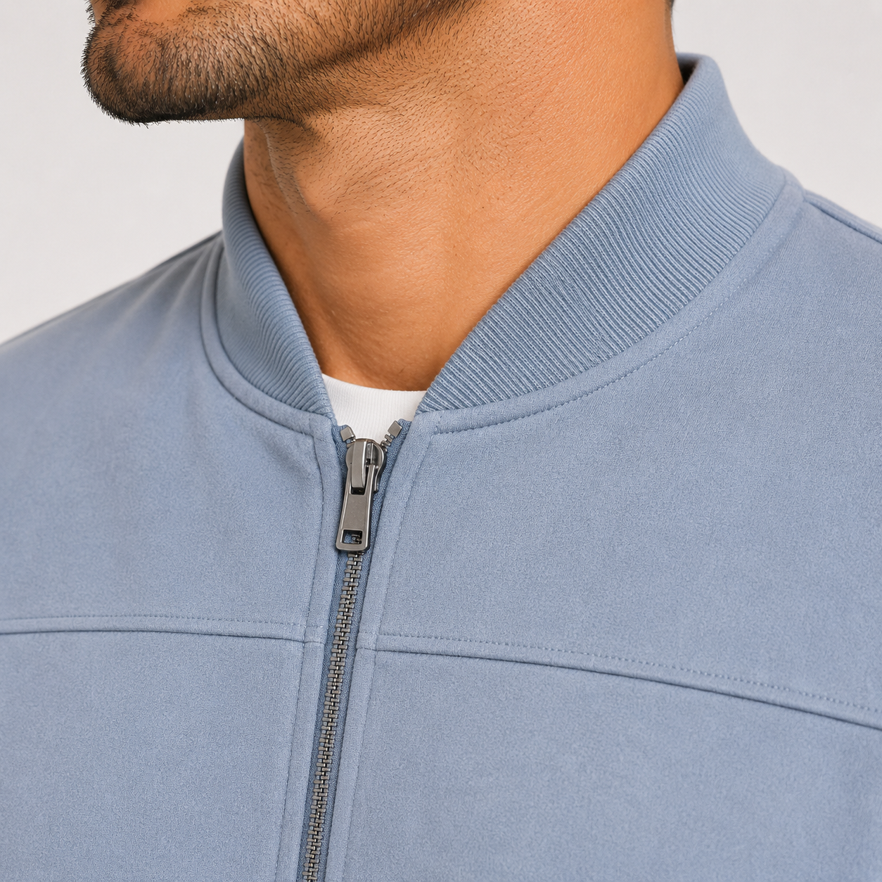 Close-up of a man wearing a light blue zip-up jacket with a ribbed collar, showing the zipper and part of his neck and chin.