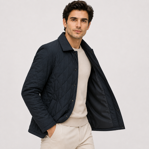 A man wearing a dark navy quilted jacket over a light beige sweater and matching trousers, photographed against a plain light gray studio background.