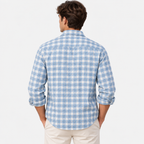 A man viewed from the back wearing a light blue and white gingham plaid long-sleeve button-down shirt with cream pants, set against a plain white studio background.
