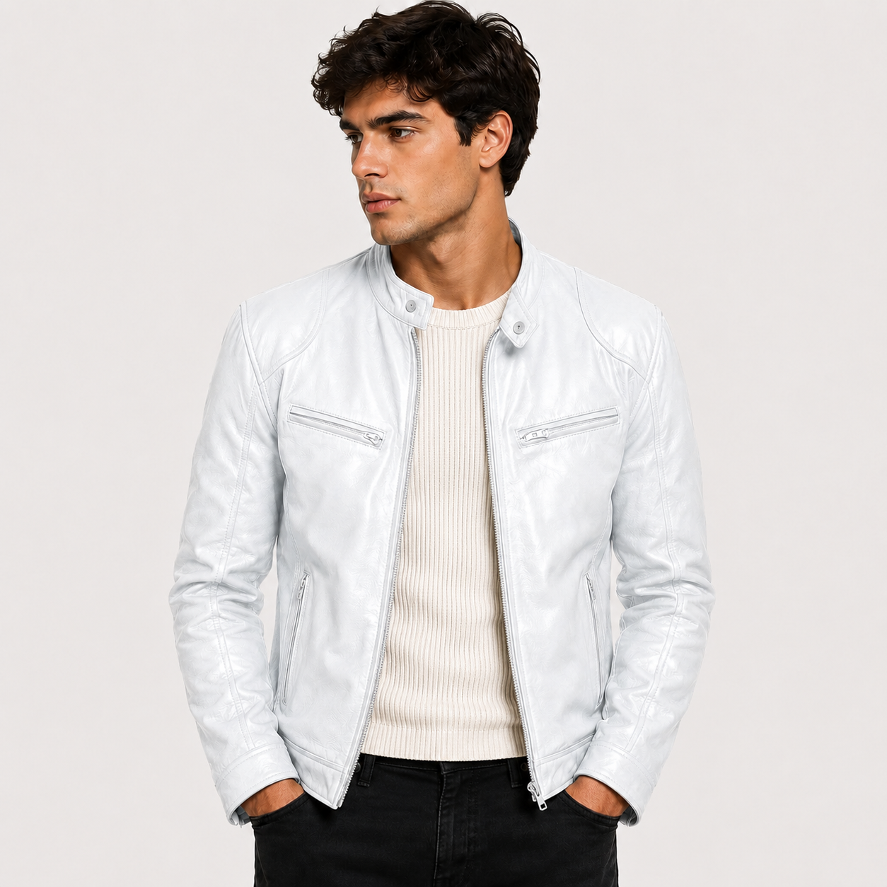 A man wearing a white leather jacket over a cream ribbed sweater and black pants, photographed against a light gray studio background.