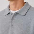 Close-up of a person wearing a light gray textured polo shirt over a white undershirt, showing the collar, three buttons, and part of the neck against a plain light background.