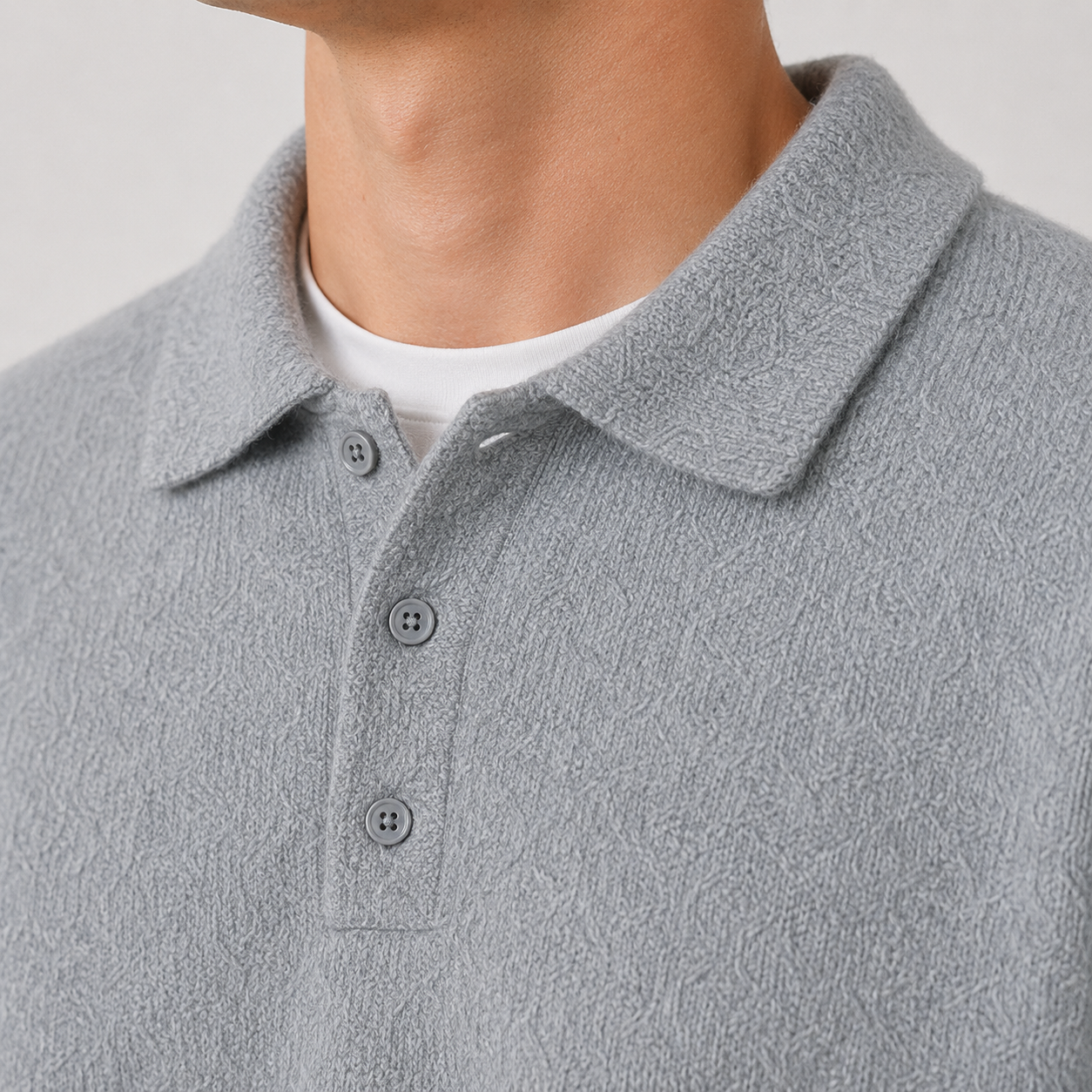 Close-up of a person wearing a light gray textured polo shirt over a white undershirt, showing the collar, three buttons, and part of the neck against a plain light background.