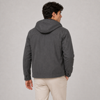 A man wearing a dark gray hooded jacket, shown from the back, paired with beige trousers, against a light gray studio background.