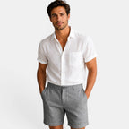Man wearing a white shirt and gray shorts on a plain background