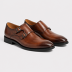 A pair of men's brown leather double monk shoes with black soles, displayed on a light gray background.