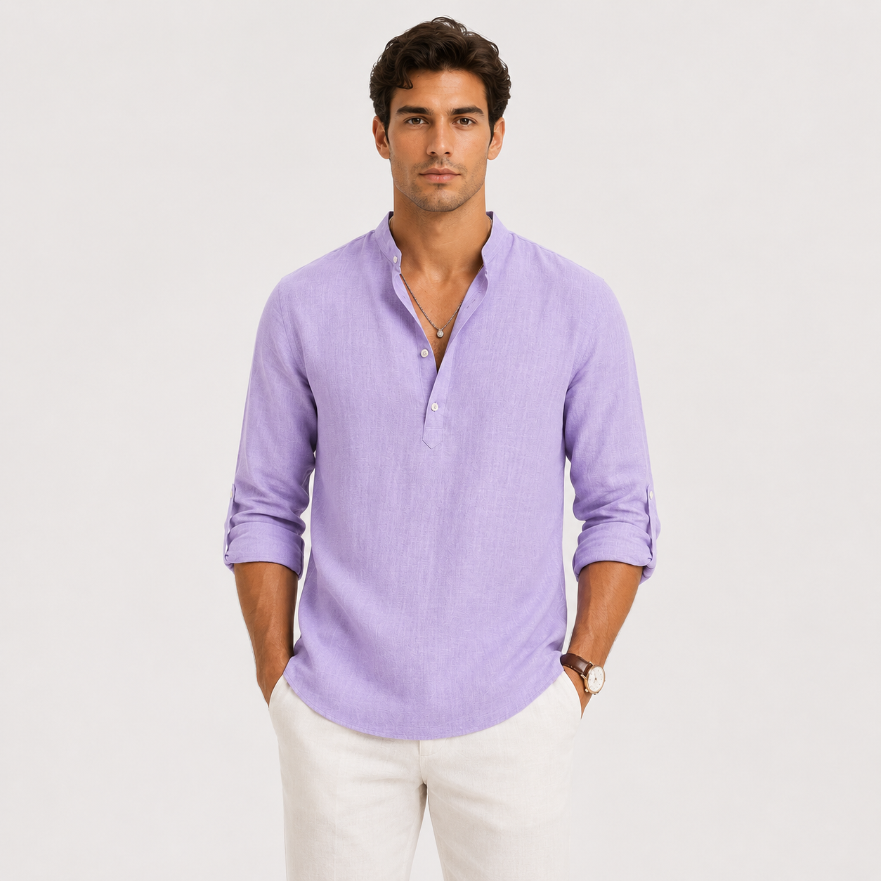 A man wearing a light purple long-sleeve linen henley shirt with white pants, standing against a light gray studio background.
