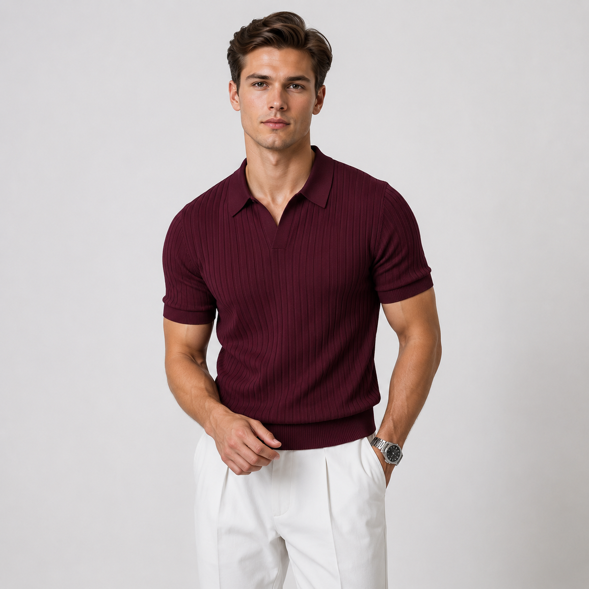A man wearing a short-sleeve ribbed polo shirt in deep burgundy with white trousers, standing against a light gray studio background.
