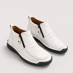 A pair of white leather ankle boots with black side zippers, black soles, and brown lining, shown on a light gray background.
