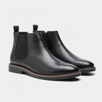 A pair of black leather Chelsea boots with elastic side panels and pull tabs, shown from a three-quarters angle on a light gray background.