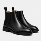A pair of black leather Chelsea boots with elastic side panels and pull tabs, shown on a light gray studio background.