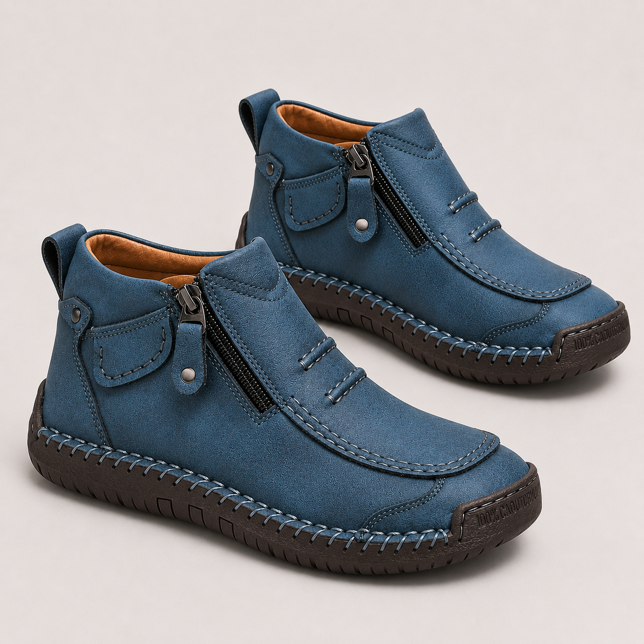 A pair of blue suede ankle boots with dark brown soles, side zippers, and decorative stitching, displayed on a light beige background.