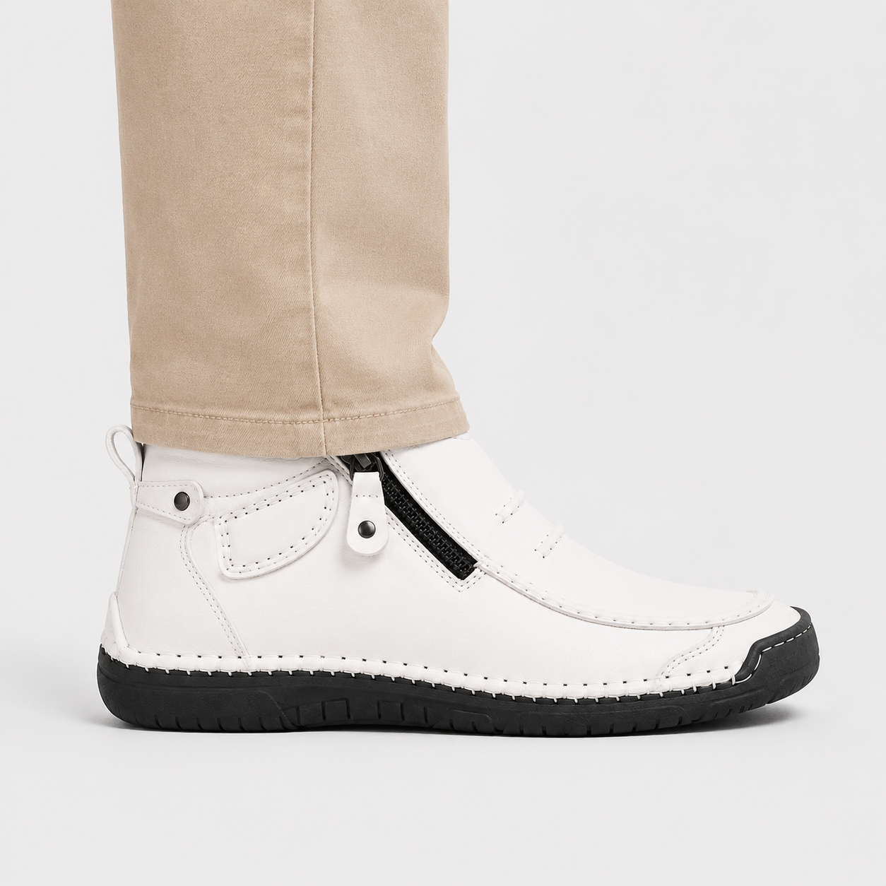 A white ankle boot with a black sole and zipper detail, shown on a model's foot with beige pants against a light gray background.